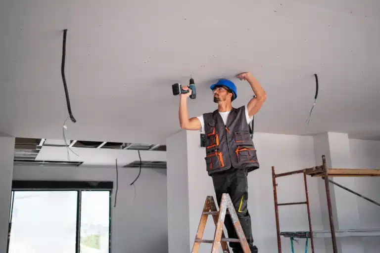 Pose de plafond en placo par un ouvrier sur échelle à Amiens.